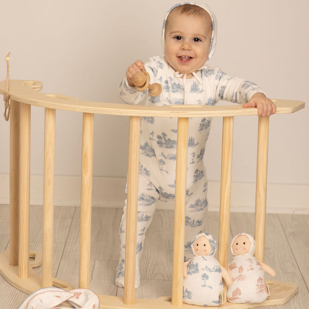 Baby standing on a wooden crib with floral pajamas and smiling.